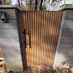 Installer fitting teak fluted cladding panels into a sliding gate frame at a residential entrance.