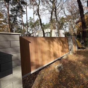 Teak WPC fluted cladding gate panel with vertical slats in a metal frame between concrete pillars.